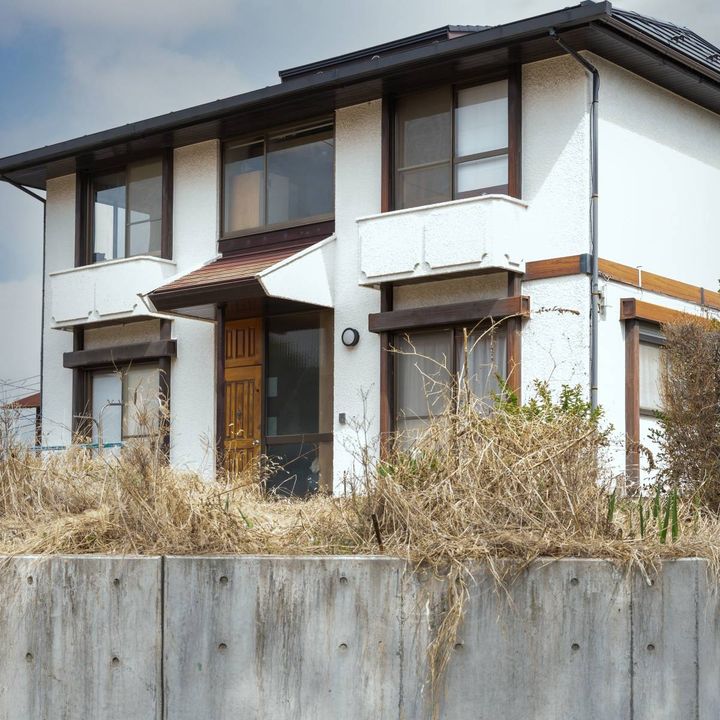 草が生い茂る庭に囲まれた、白い壁の古い二階建て一軒家