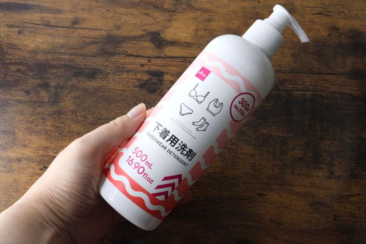 女性の手がダイソーの下着用洗剤の白いポンプ式ボトルを横向きに持っている