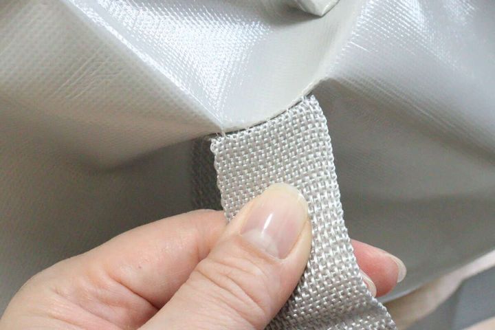 女性の手がジッパー付バッグの持ち手と本体の接続部分を引っ張っている