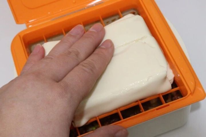 麻婆豆腐職人の容器に豆腐をパックごと押し込んでいる手元