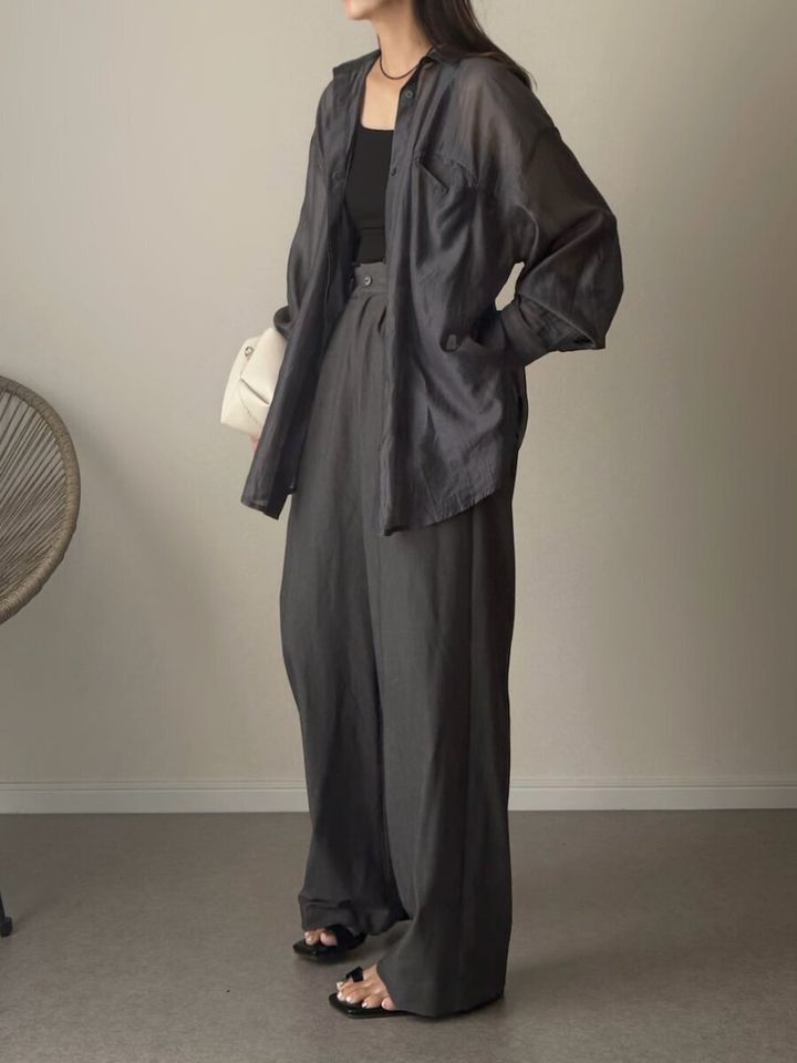 黒のシアーシャツとワイドパンツを着用し、白いショルダーバッグを持つ女性