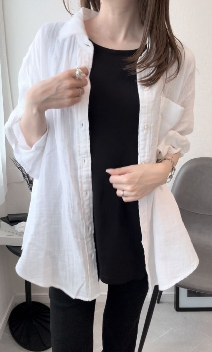 黒いトップスの上に白いシャツを羽織った女性