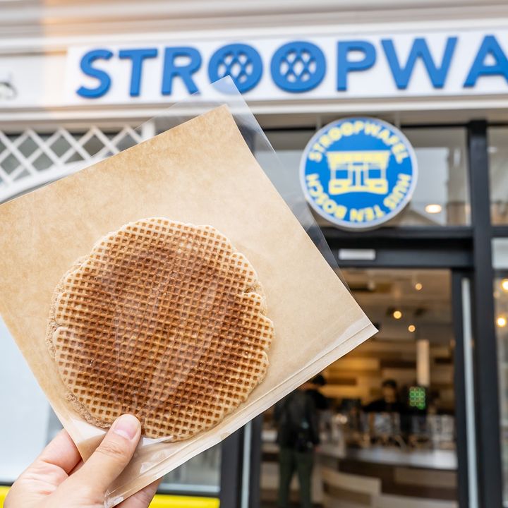 STROOPWAFELのロゴ看板の前で掲げた袋入りのストロープワッフル