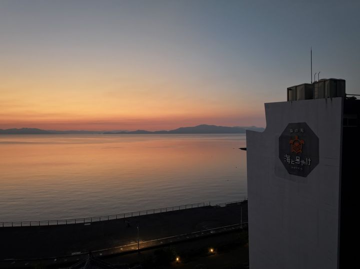 「湯の児温泉 海と夕やけ」の看板と夕焼けの実景