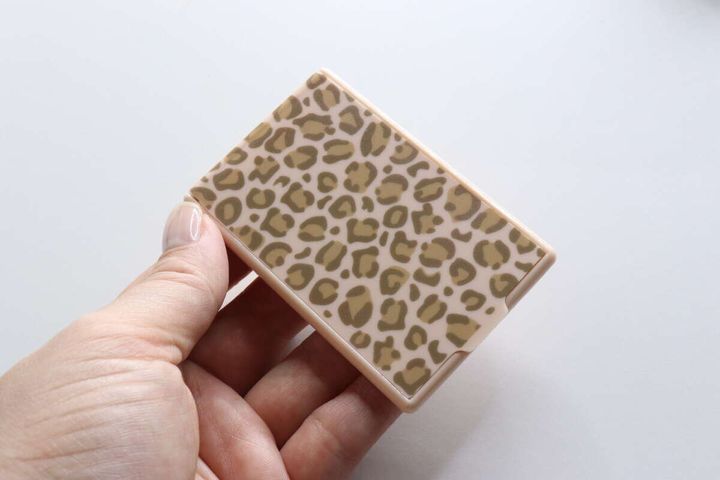 女性の手に持たれたヒョウ柄デザインのコンパクトミラー