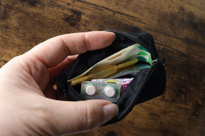 女性の手が黒いキーホルダーポーチを開き、中に絆創膏や常備薬が入っている様子
