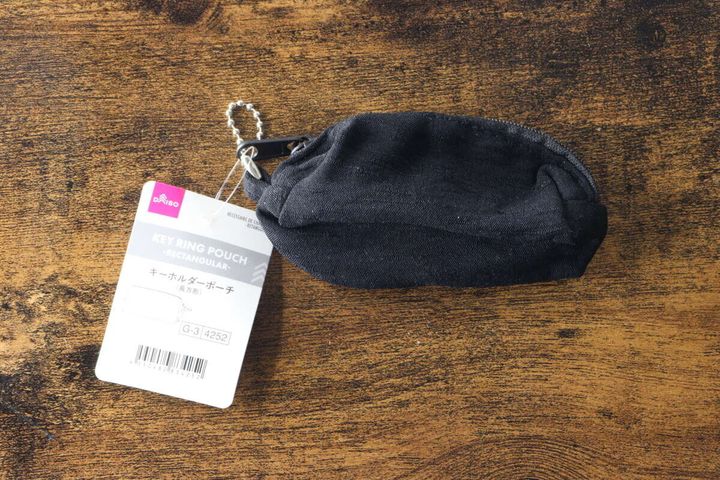 黒い長方形のキーホルダーポーチが木目のテーブルに置かれ、商品タグが付いている俯瞰写真