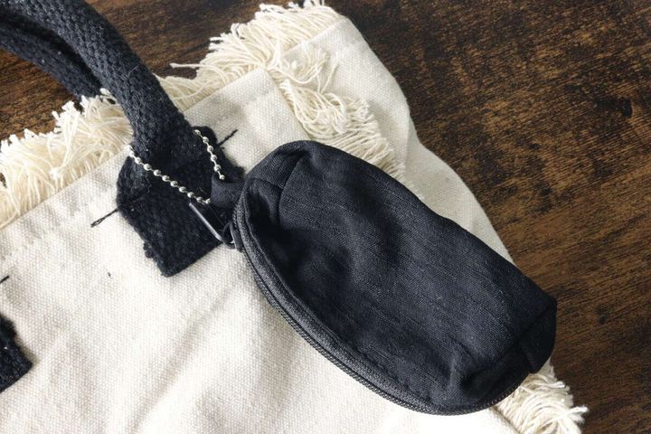 白いフリンジ付きのバッグの持ち手に、黒いキーホルダーポーチがボールチェーンで取り付けられている