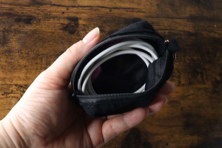 女性の手が黒いキーホルダーポーチを開き、中に白い充電ケーブルが丸めて収納されている様子
