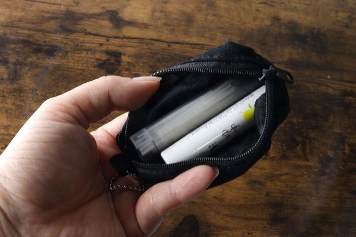 女性の手が黒いキーホルダーポーチを開き、中にリップクリームとデンタルピックが入っている様子