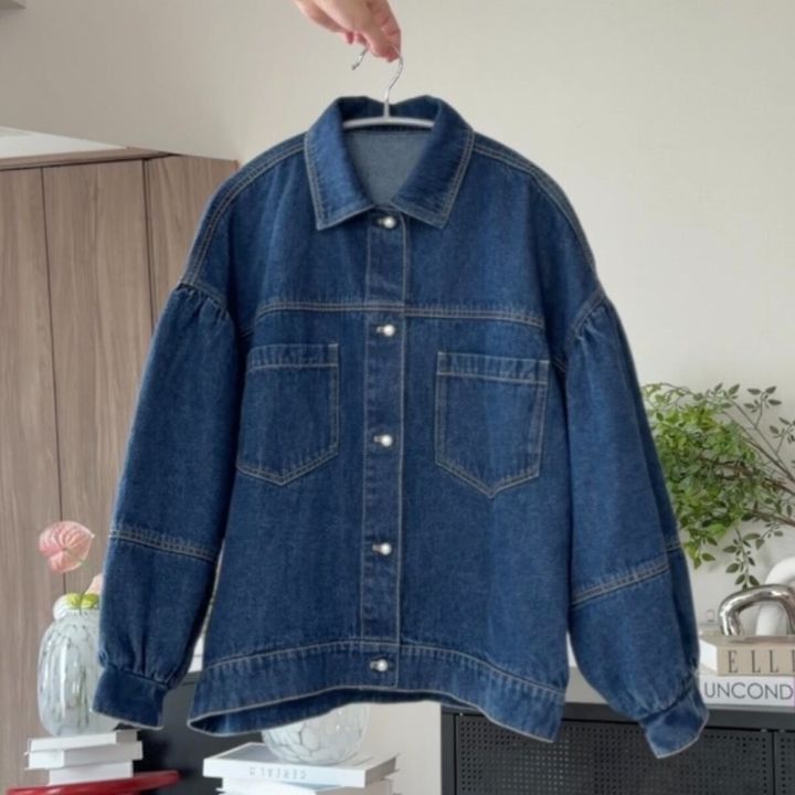パールボタンと丸い袖が特徴のデニムジャケットを手に持っている