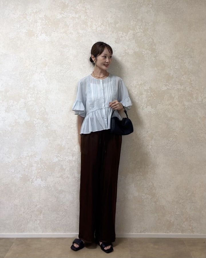ブルーのフリルシャツと黒バッグを着用した女性の全身