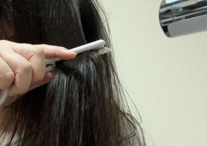 女性が白いコームで髪を挟みドライヤーを当ててブローしている様子