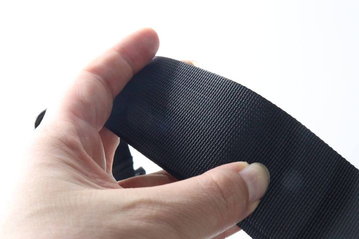 幅広の黒いショルダーバッグストラップを指でつまむ