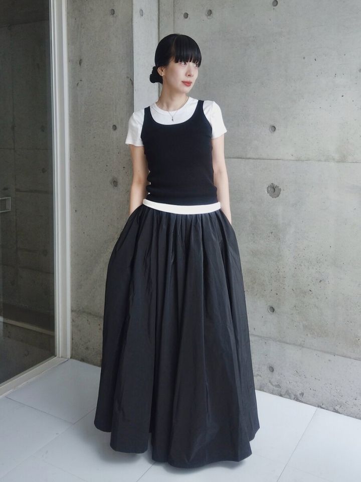 白Tと黒タンクトップを重ね着し、黒いロングスカートを穿く女性