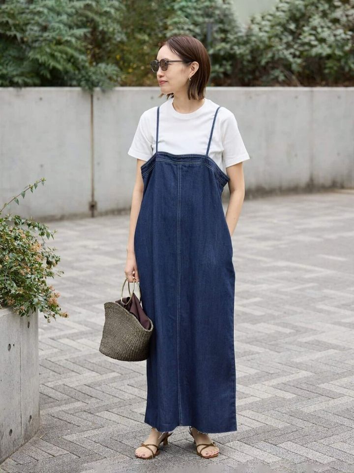 白Tにデニムのジャンパースカートを着て、カゴバッグを持つ女性