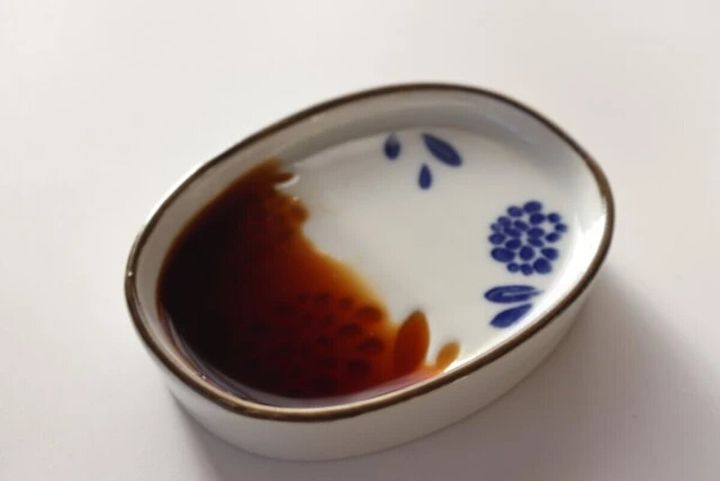 白いななめ醤油皿に醤油が注がれ、傾斜に溜まっている