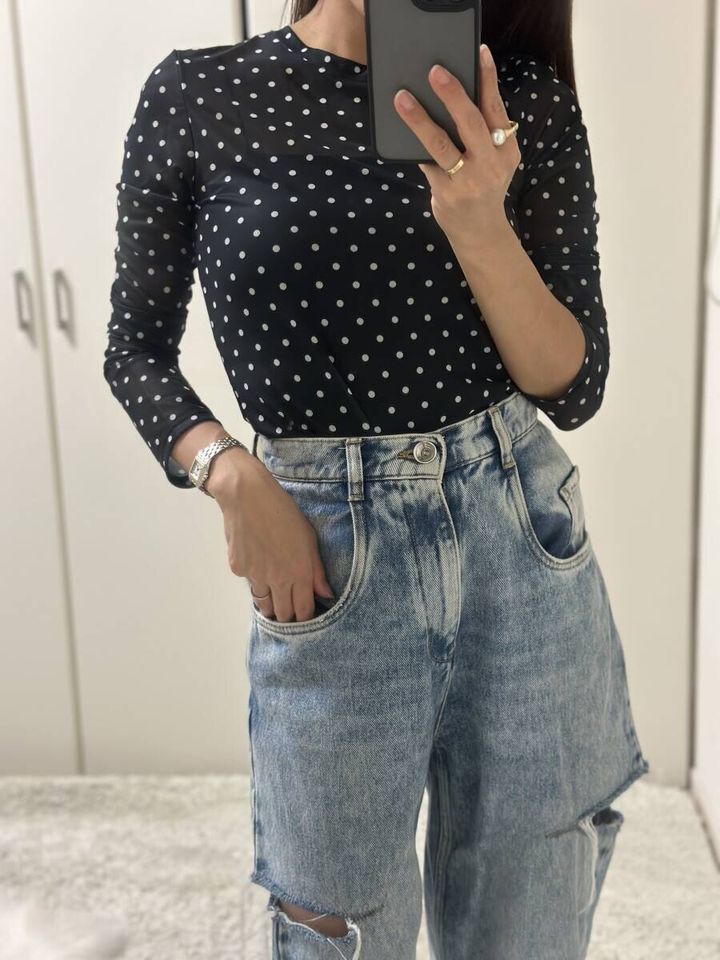 黒いドット柄のシアーTシャツとダメージデニムを着用し、スマホを持つ女性のウエストアップ