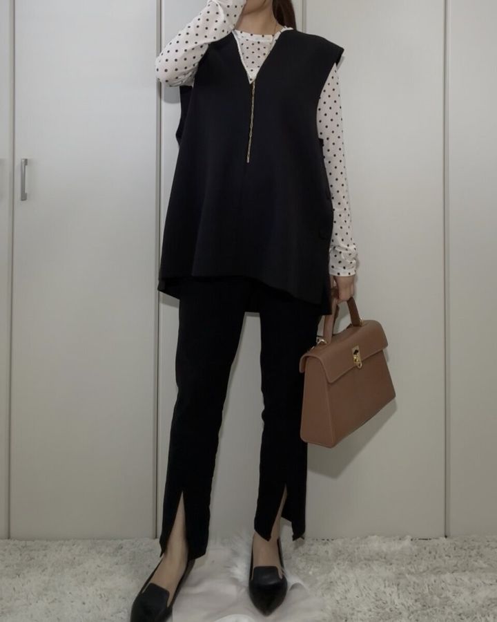 白いドット柄のシアーTシャツに黒いベストとパンツ、茶色のハンドバッグを合わせた全身コーデの女性