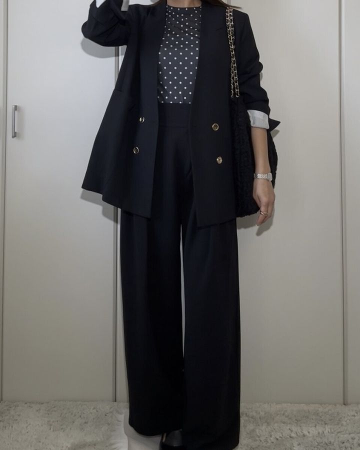 黒いドット柄のシアーTシャツに黒いジャケットとワイドパンツ、黒いバッグを合わせた全身コーデの女性