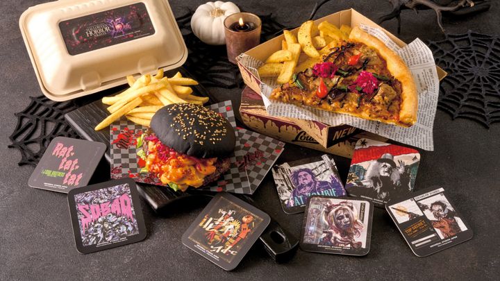 黒いバンズのハンバーガーとケイジャンチキン・ピッツァ、歴代ゾンビや楽曲ジャケットをデザインした15周年コースターを並べたセット