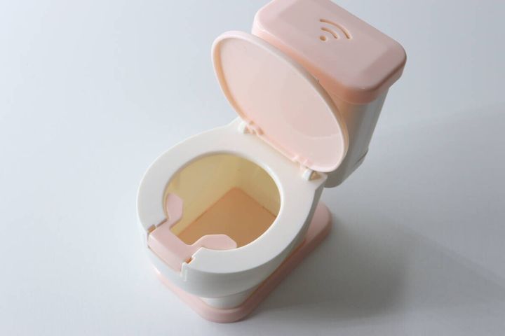 ピンクと白の便器型スマホスタンドの便座が開いており、中にスタンド部分が見える