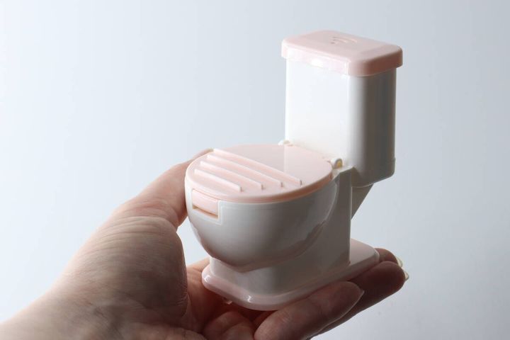 女性の手のひらに乗せられた、ピンクと白の便器型スマホスタンド