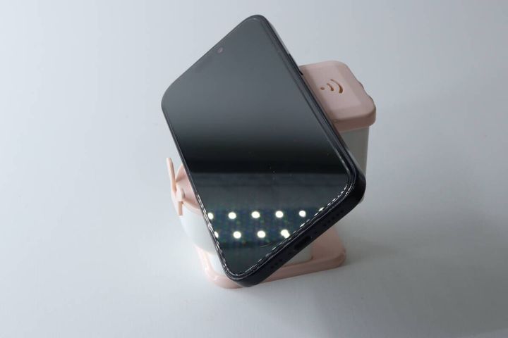ピンクと白の便器型スマホスタンドに黒いスマートフォンが横向きに立てられている