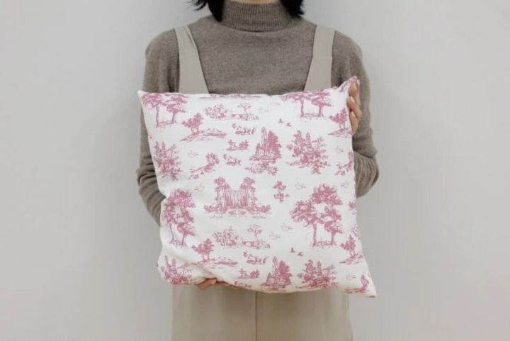女性が両手でピンク色のトワルドジュイ柄クッションを抱えている