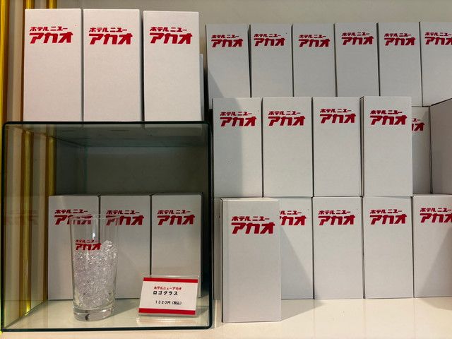 「ホテルニューアカオ」のロゴが入ったグッズと箱が並ぶ売店の棚