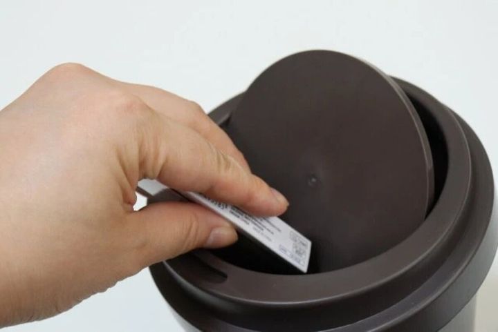 コーヒーカップ型ゴミ箱のフタを開けて物を捨てる手元