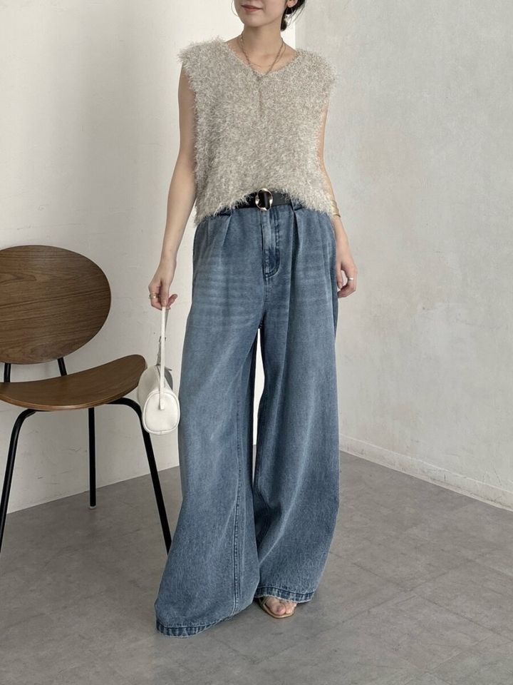 ベージュのフリンジニットベストとワイドデニムを着用し、白いミニバッグを持つ女性