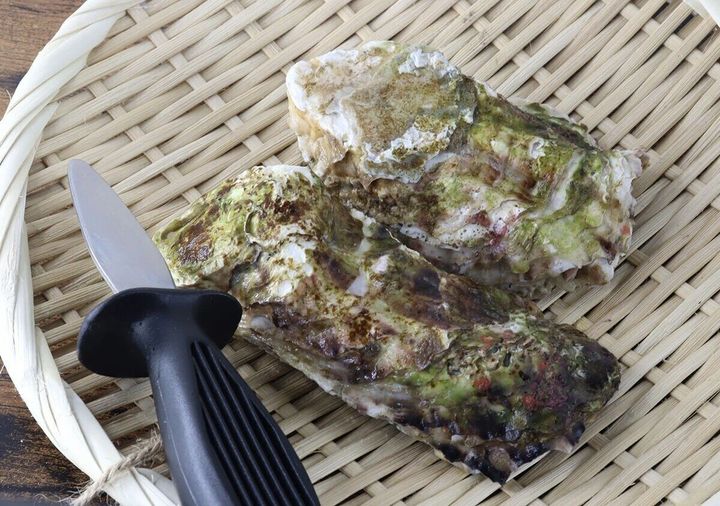黒い柄の貝むきナイフと岩牡蠣が竹ざるに乗っている