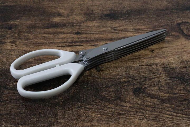 白い持ち手の5枚刃キッチンバサミが木目調の台に置かれている