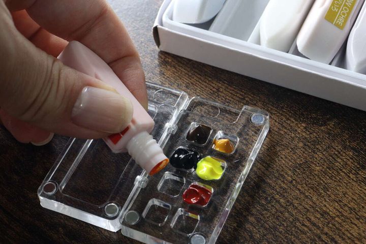 透明なパレットのくぼみにチューブ絵の具を絞り入れている手元