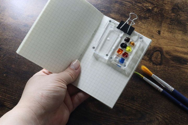 開いたスケッチブックのページにクリップで固定された絵の具パレット
