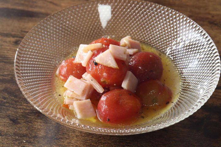 ガラスの器に入った、ミニトマトと角切りハムのマリネ。ハーブが散らされている