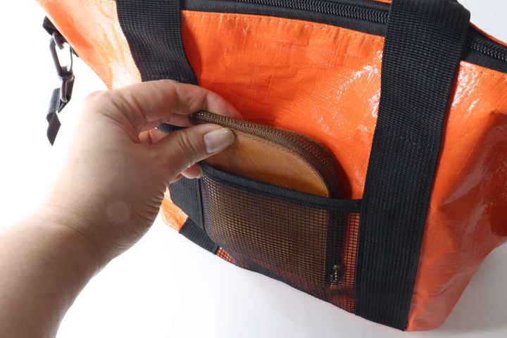 手がトートバッグの前面にあるメッシュポケットに茶色い折り財布を入れている