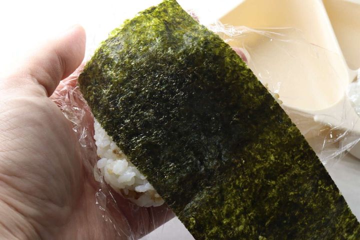 ラップで包んだおにぎりに海苔を巻いている手元
