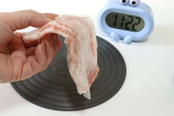 ラップに包まれた肉の塊を、黒い解凍プレートの上に置こうとしている手元と、奥に青い目覚まし時計
