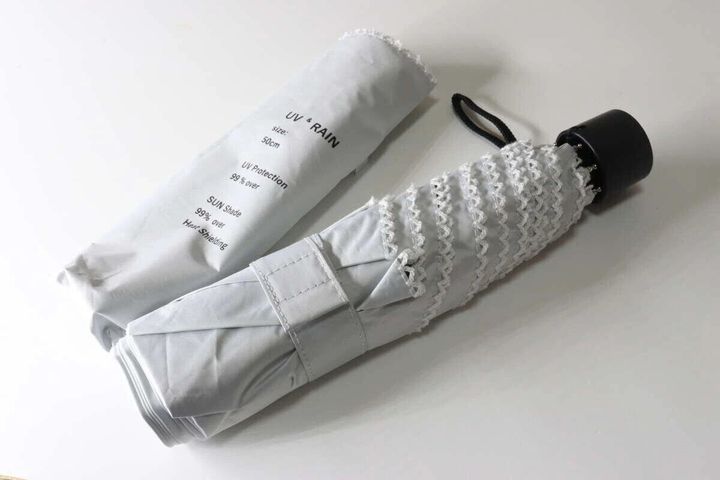 白い収納袋と、白いピコレースがあしらわれた折りたたみ傘が畳まれた状態で置かれている