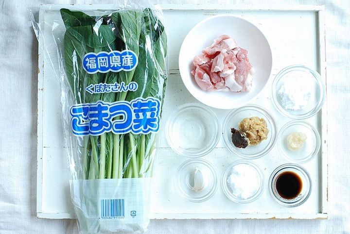 白い木目のテーブルに並べられた小松菜の袋と豚こま切れ肉、各種調味料