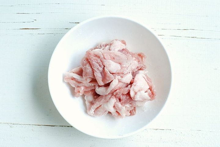 白いボウルに入った片栗粉がまぶされた豚こま切れ肉