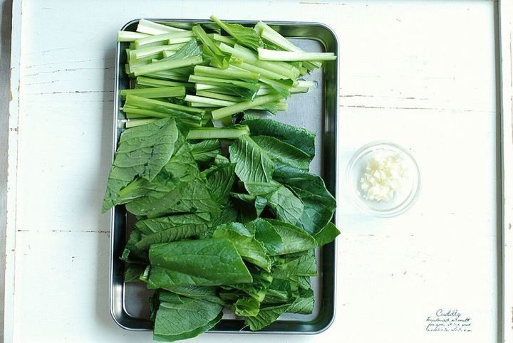 銀色のバットにざく切りされた小松菜の茎と葉、横にみじん切りにんにく