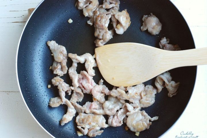 黒いフライパンで炒められている豚こま切れ肉と木製のへら