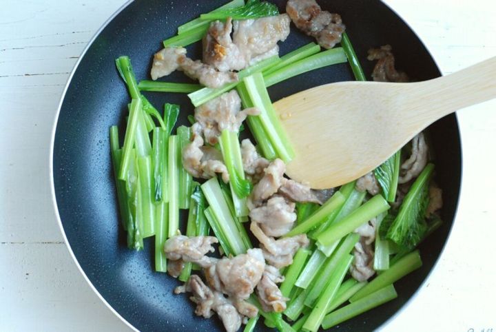 フライパンで豚こま切れ肉とざく切りされた小松菜の茎が炒められている様子
