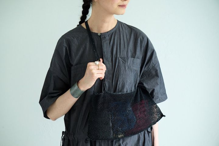 えみおわすの葛網バッグを斜め掛けし、海野毅のチタン製バングルとシルバー＆ゴールドのリングを合わせた手もと