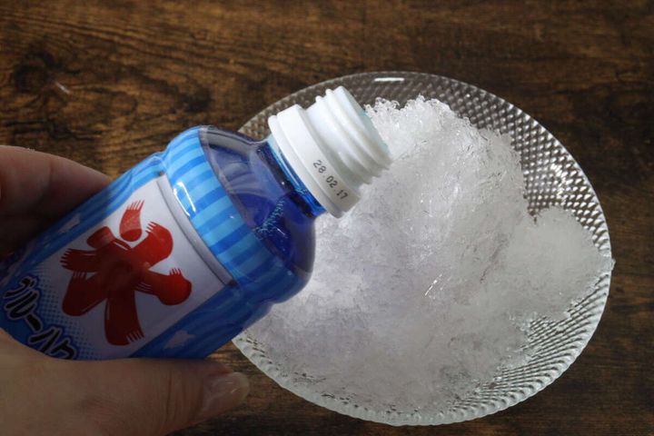 削ったかき氷にブルーハワイのシロップをかけている手元