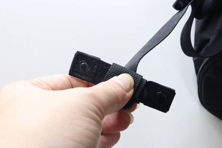 リュックの黒い調節ヒモに固定バンドを巻き付けている様子