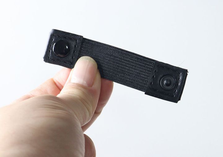 指でつまんで見せている黒いゴムバンドとスナップボタンの固定バンド